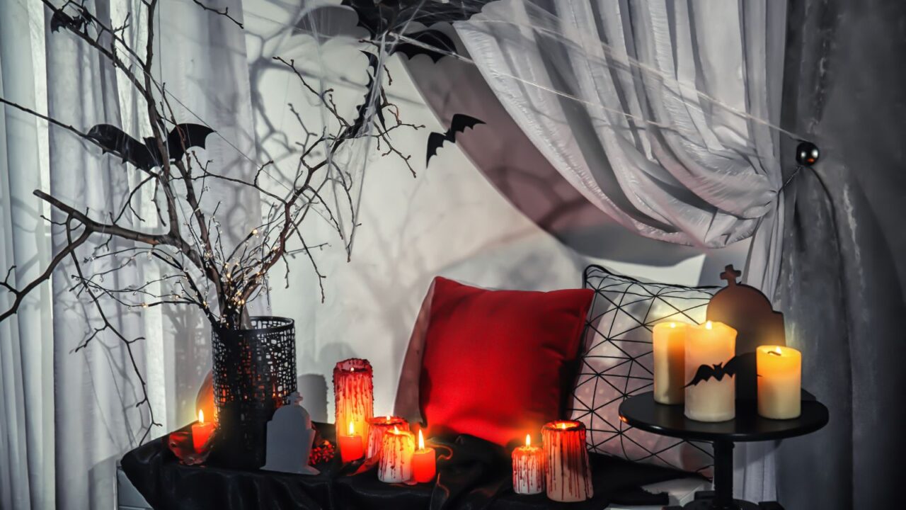 Halloween decor set up in a corner of the room. Red colored pillow, candles, dried stems, and other decor accents are used to create a spooky Halloween corner