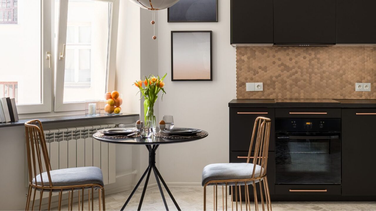 A kitchen interior with black cabinets, chrome dining chairs around a black glass table, and artwork on wall.