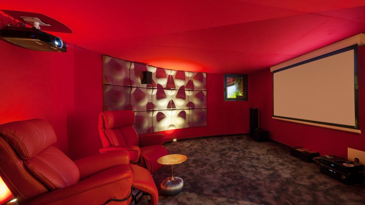 A red interior home theater with a projector, red recliners, and a small round table.