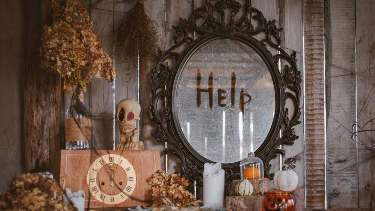 A room interior with ornate mirror, skull, vintage clock. candles, dies flowers in a bottle, and pumpkins.