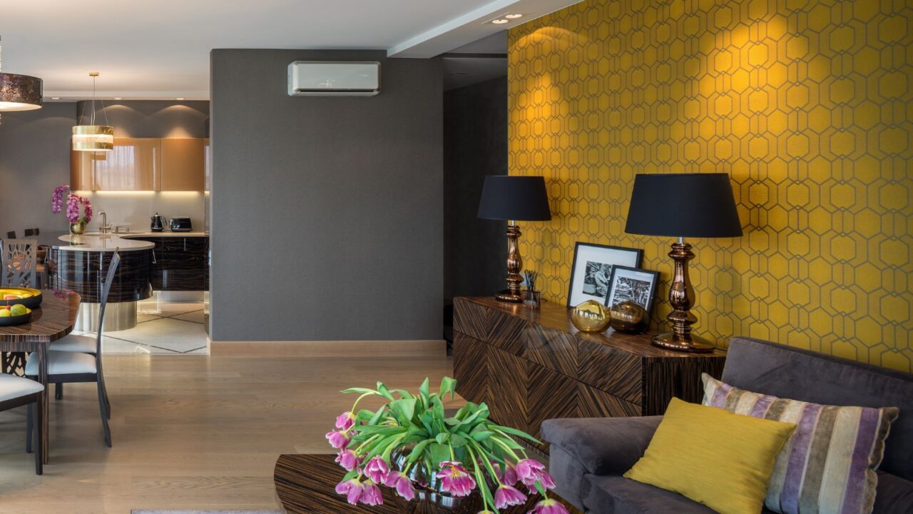 A living room interior with patterned mustard yellow accent wall, a wooden console with lamps and decor, and gray sofa.