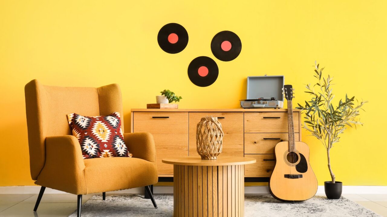 Retro inspired yellow beautiful living room with chest of drawers, armchair, acoustic guitar and olive tree. Retro cushion and coffee table.