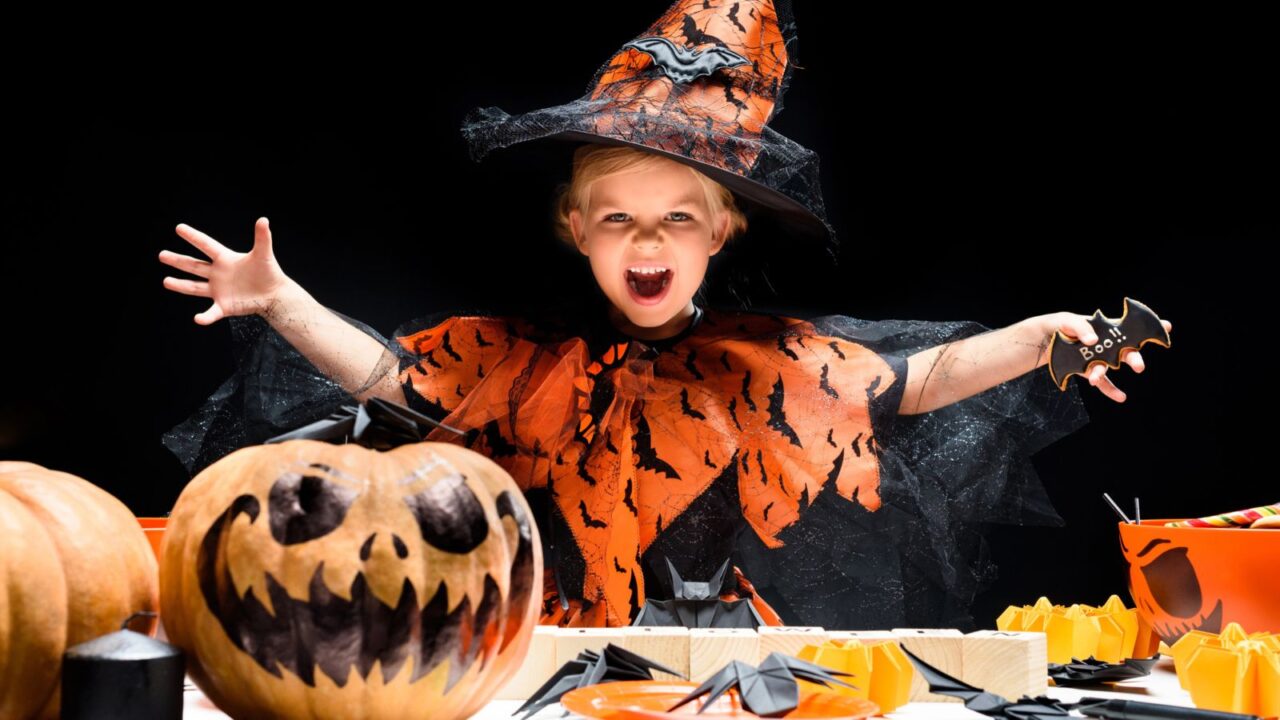 A kid dresses up as a witch for Halloween. She has a table filled with spooky items.