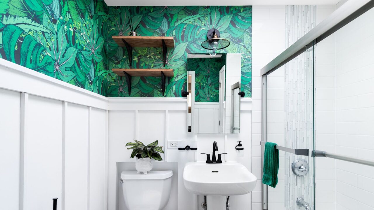 A bright white bathroom with a beautiful, colorful green leaf wallpaper.