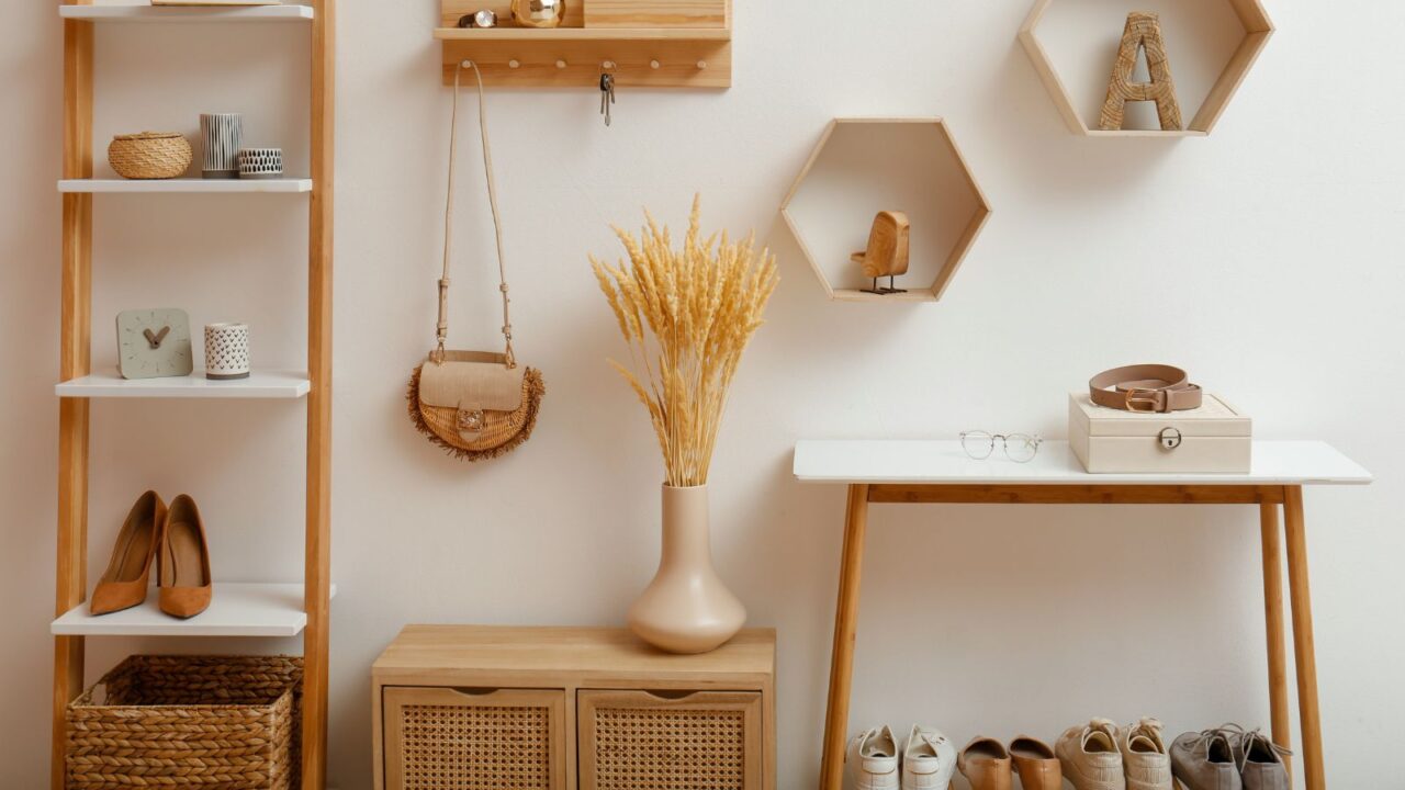 A wooden key holder, vase with dried wheat, and a wooden console table with shoes, glasses, and a box on it.