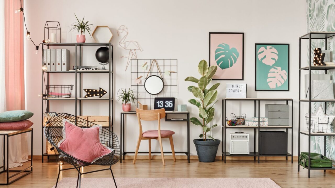 A stylish home office interior with a desk and chair, shelves, a mesh chair, and frames on a white wall.