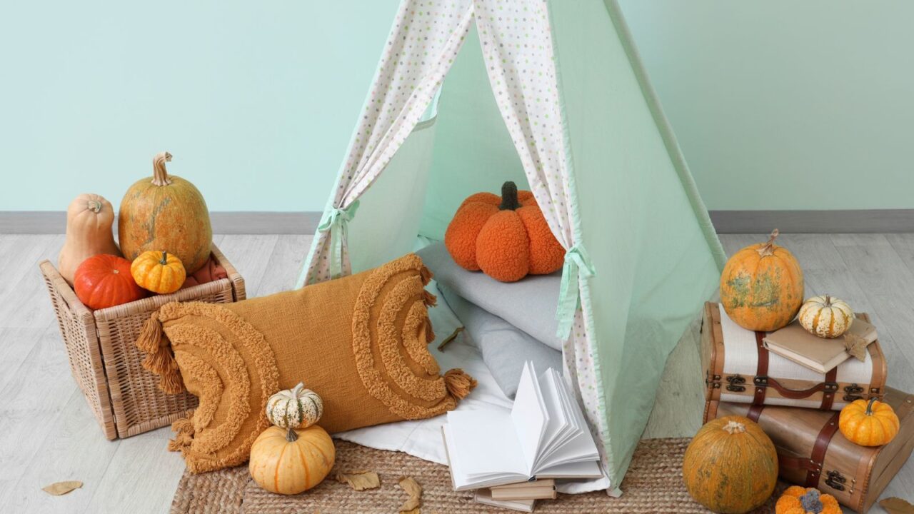 Interior of children's play room with tent, pumpkins, books, suit cases, leaves, and fall decor