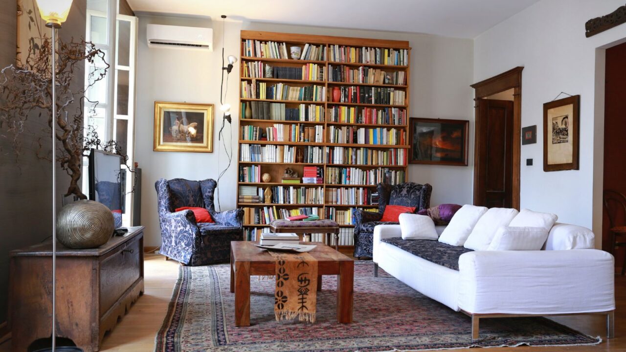 A home library interior with a couch, wooden table, art work, and floor to ceiling wooden bookshelf.