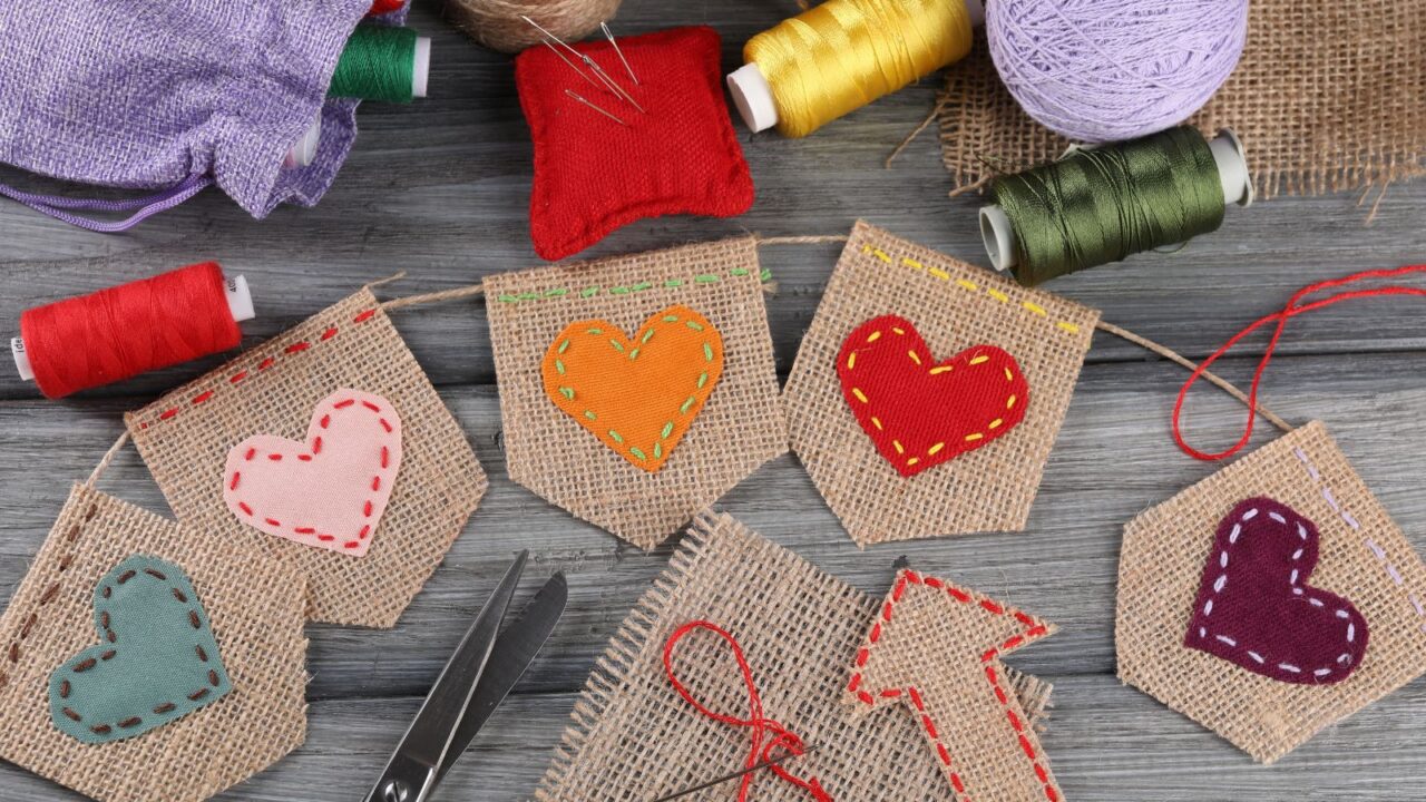 Bunting flags made with burlap fabric and sewing tools on grey wooden table, flat lay.