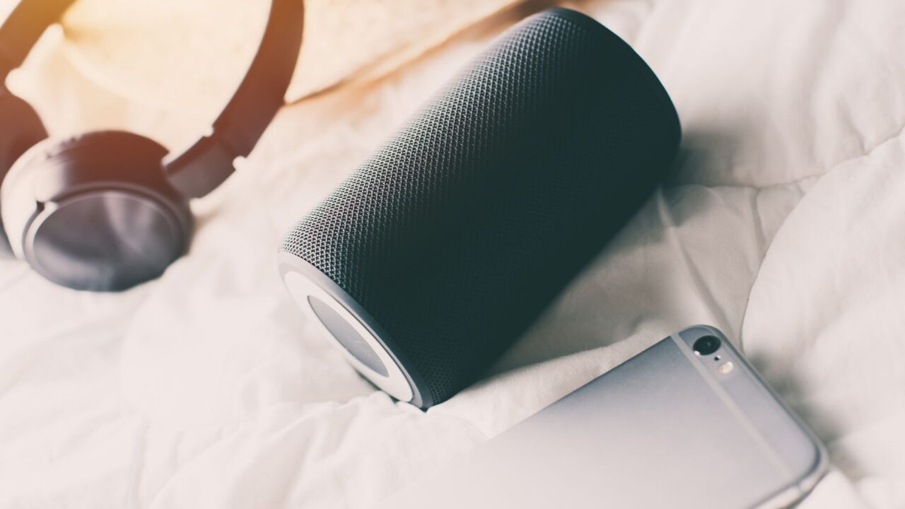 wireless bluetooth speaker, headphones, and a mobile on a bed