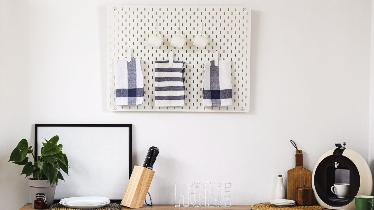 Pegboard on white wall in modern kitchen with mugs hanging on it.