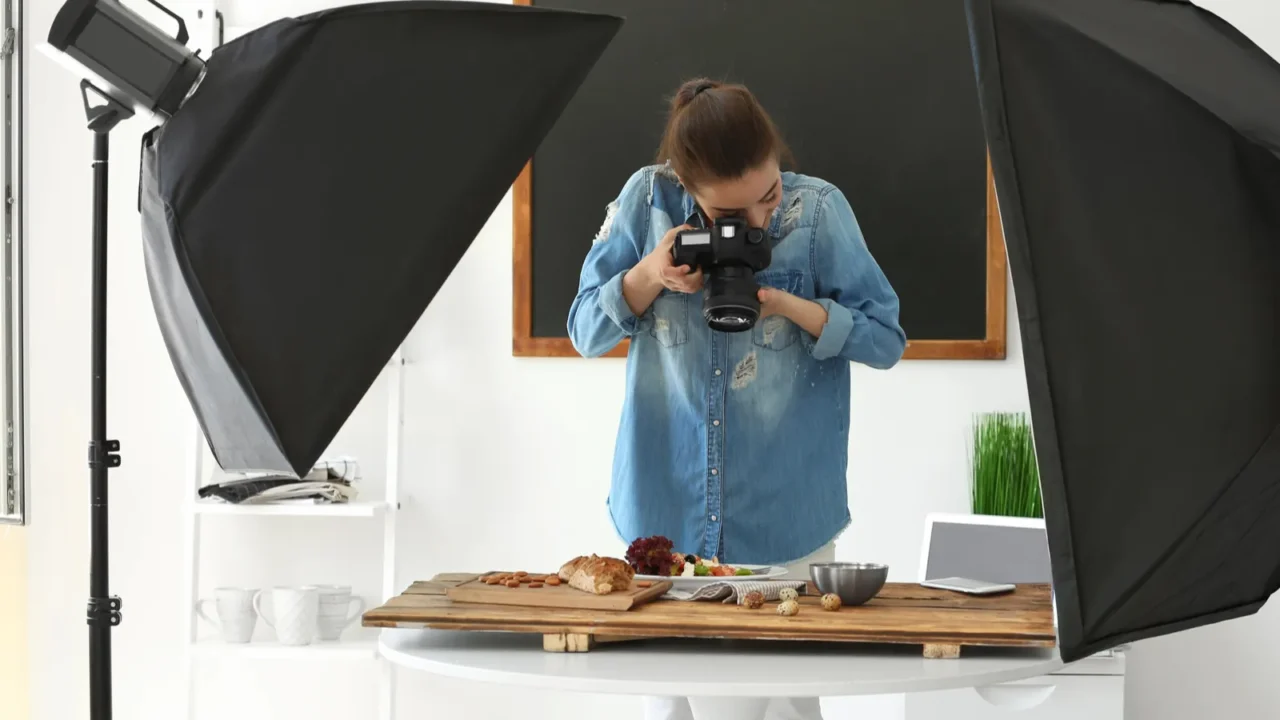 Young woman with professional camera taking still life pictures in photo studio