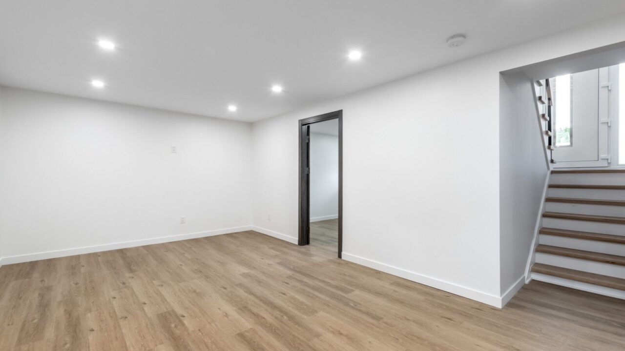 An empty well lit basement area with wooden floors and white floors