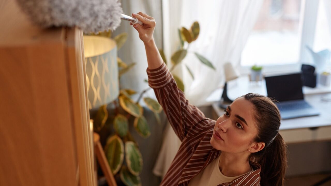 Top view shot of a woman cleaning dust from above the cupboard.