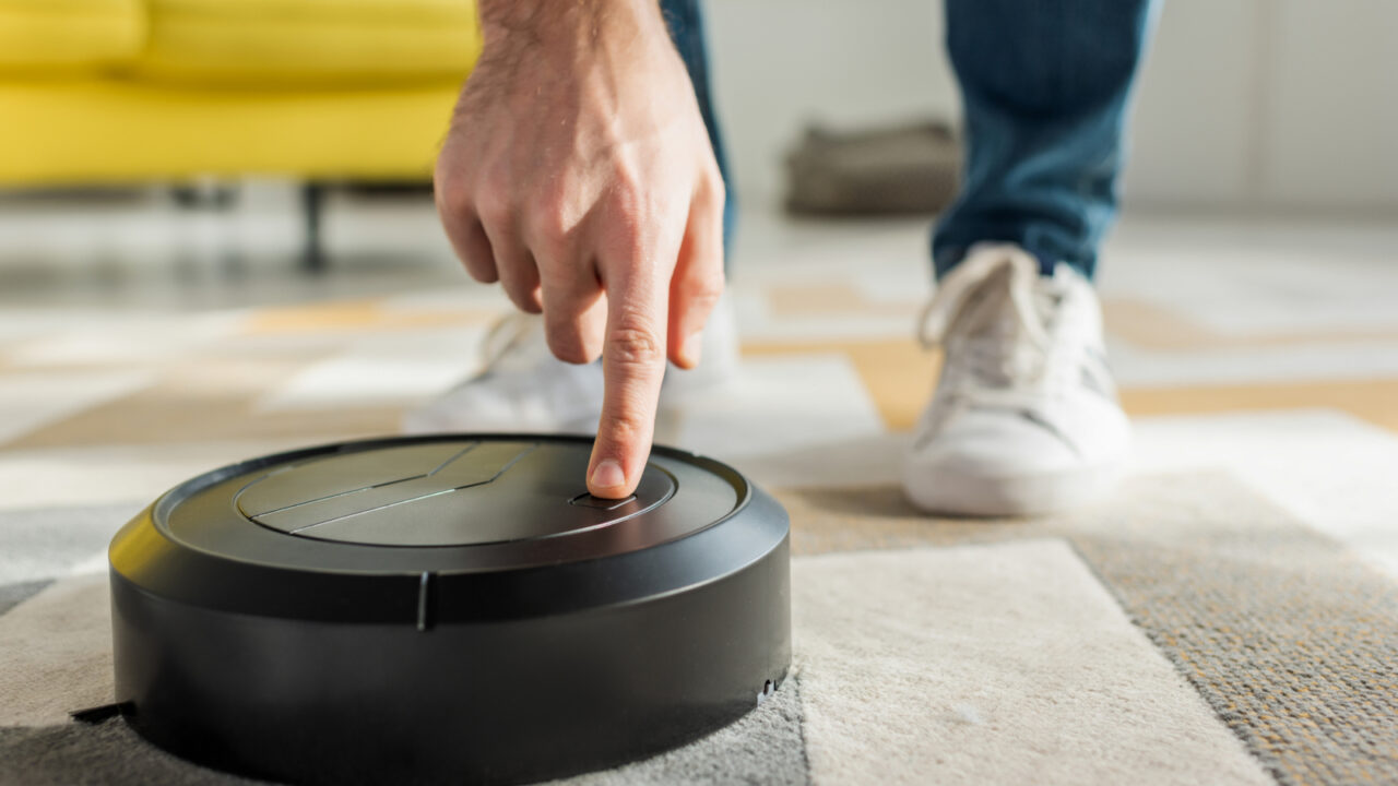 cropped view of man pointing with finger at robotic vacuum cleaner in living room