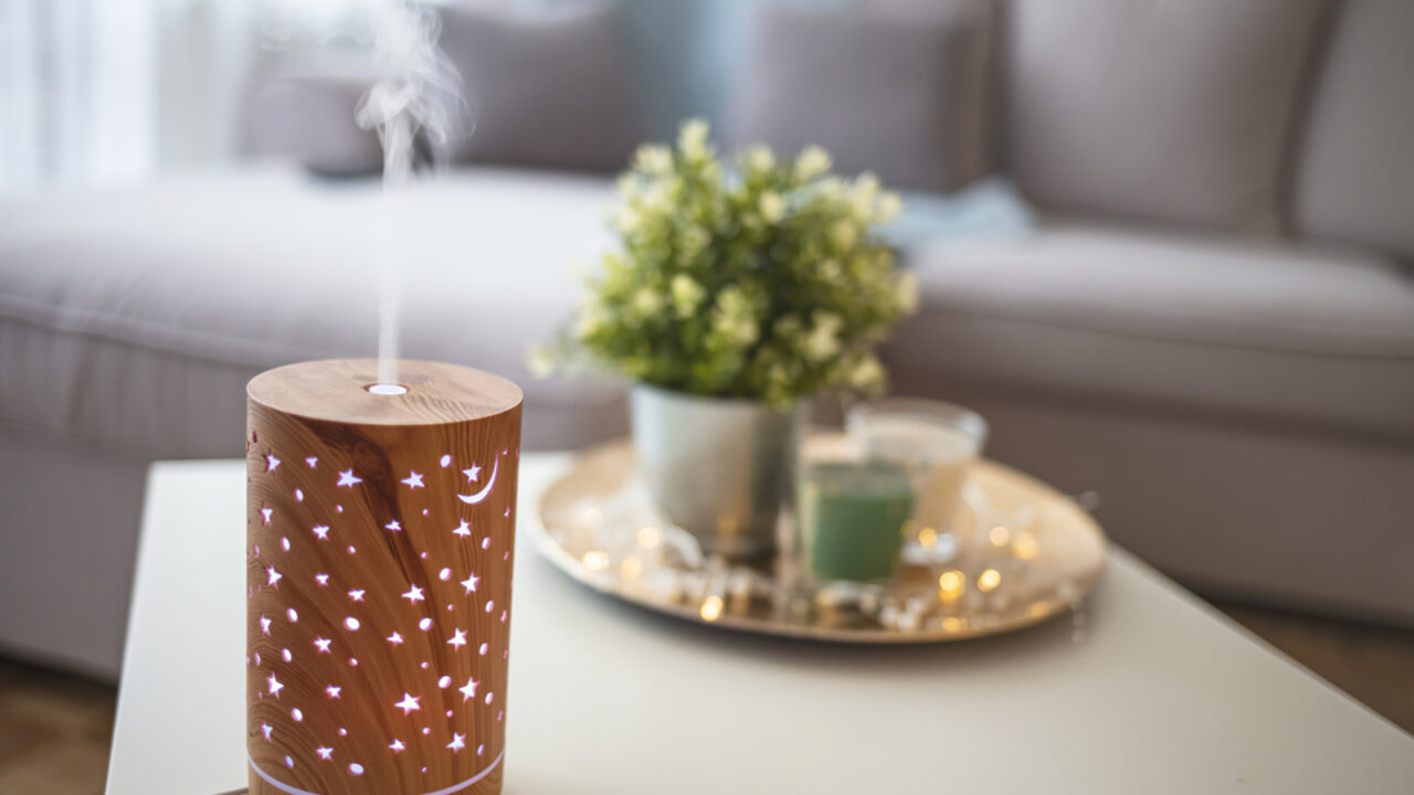 Diffuser spreading essential oils in livingroom and woman relaxing. Aroma health essence, welness aromatherapy home spa fragrance tranquil theraphy, therapeutic steam, mental health treatment