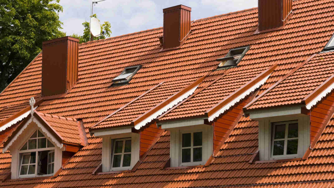 Red shingled roof of a house with multiple windows and chimneys