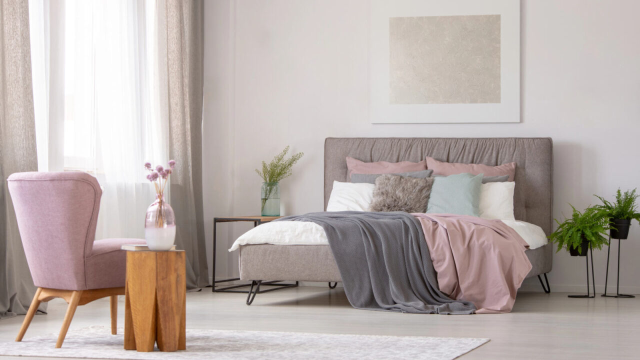 Bedroom interior in pastel gray and pink tones with pink armchair, gray poster bed and decorative plants on nightstands