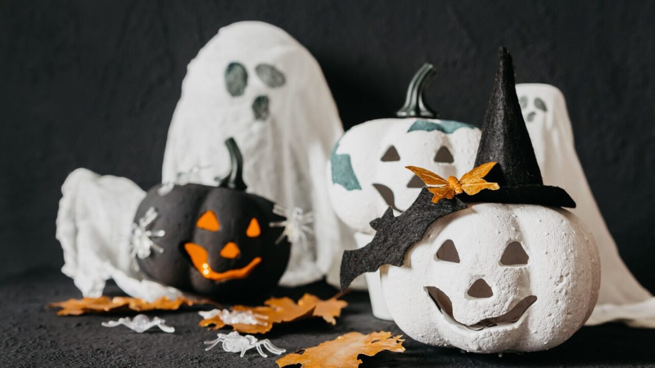 Halloween decor with carved pumpkins painted in white black and placed against black background