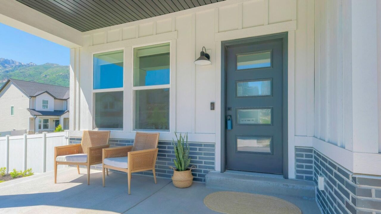 A house exterior view, showing front door, two chairs and snake plant on porch, and two windows next to the front door