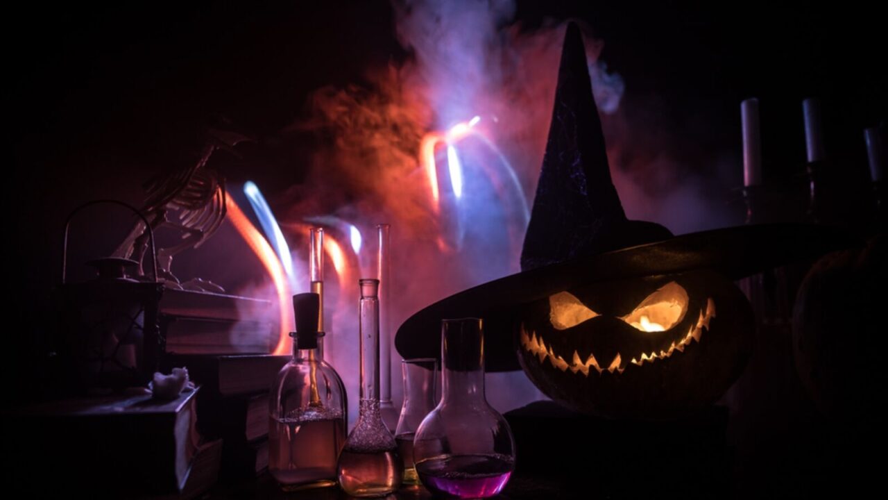 Magic potions in bottles on wooden table with books, candles, and creepy pumpkin.