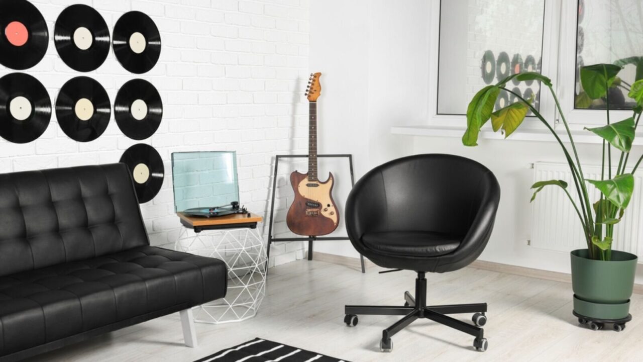 Living room decorated with vinyl records, black sofa, black chair, guitar, and a plant pot.