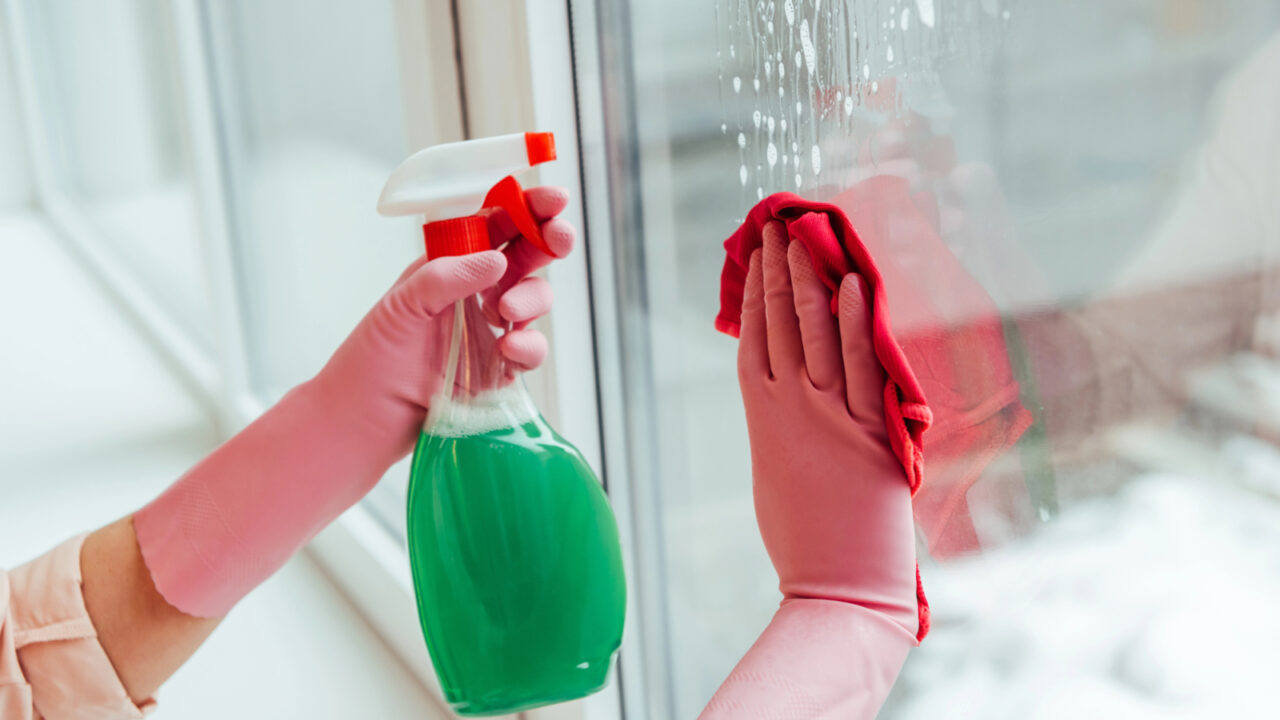 Partial view of woman in pink gloves cleaning window with spray and rag