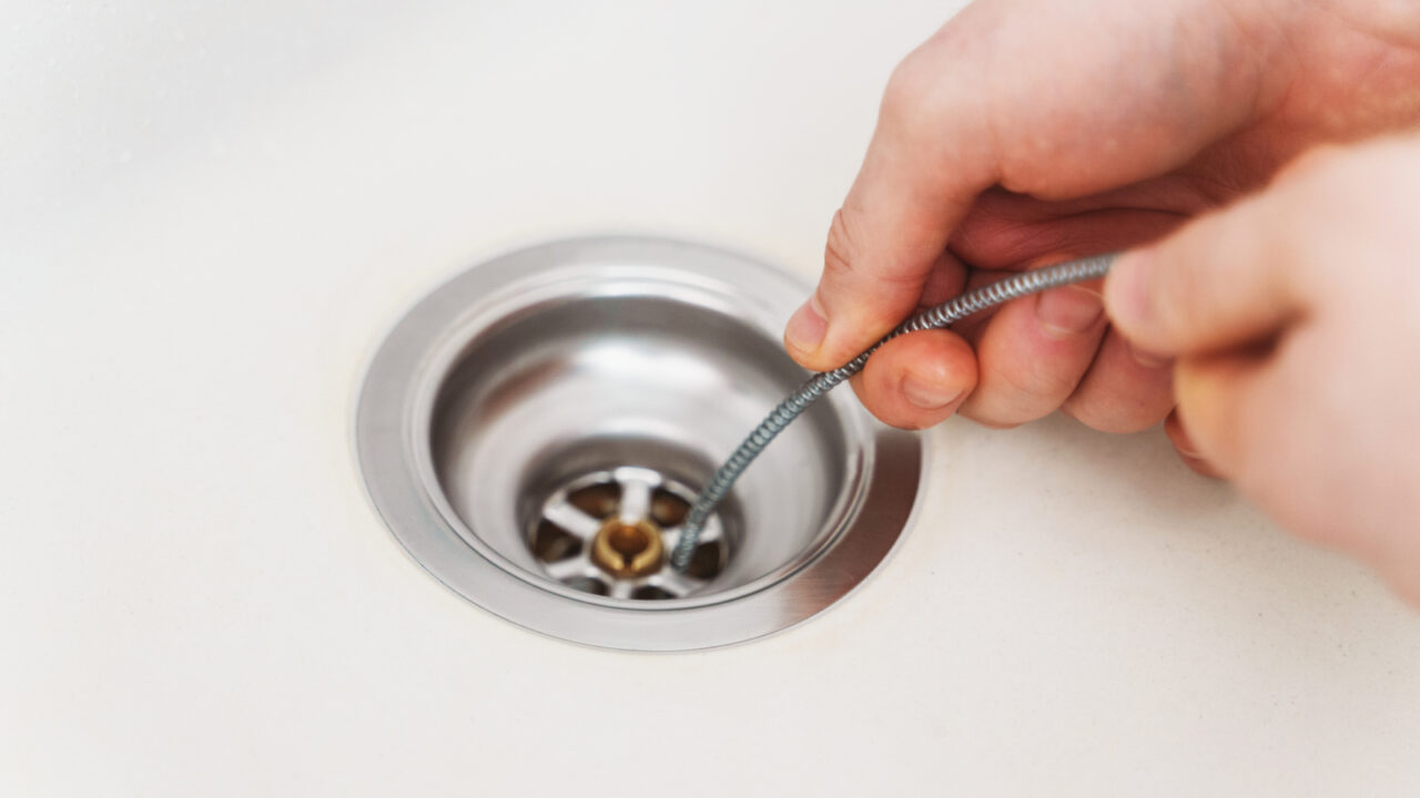 Plumber using drain snake to unclog kitchen sink.