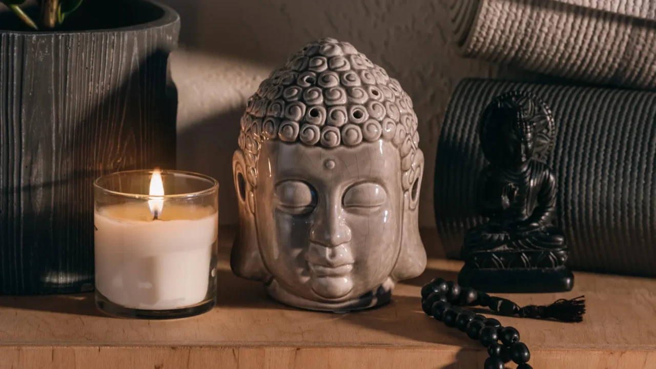 Sculptures of buddha, burning candle, and yoga mats on wooden shelf.
