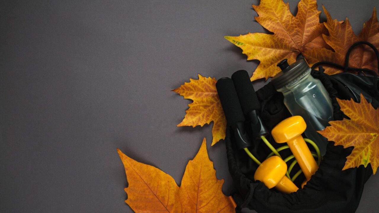 Yellow dumbbells, jumping rope, and a water bottle surrounded with dried autumn leaves