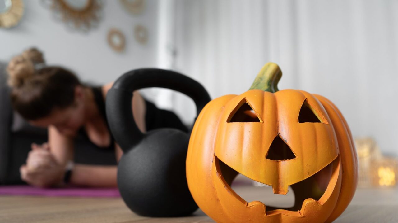 A pumpkin and kettlebell is on the floor at the front and a girl is doing a plank in the background