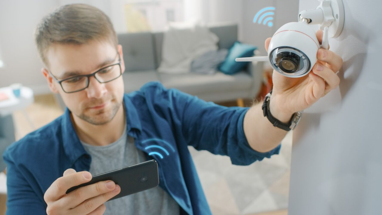 A young white man adjusting the view of security camera in his home while using smart phone