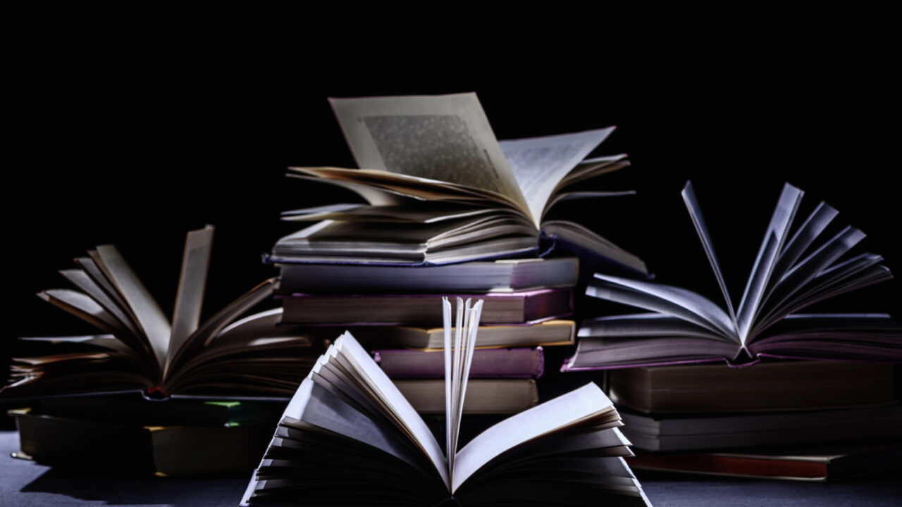 Stacks of books with opened pages on a table in front of a dark background.