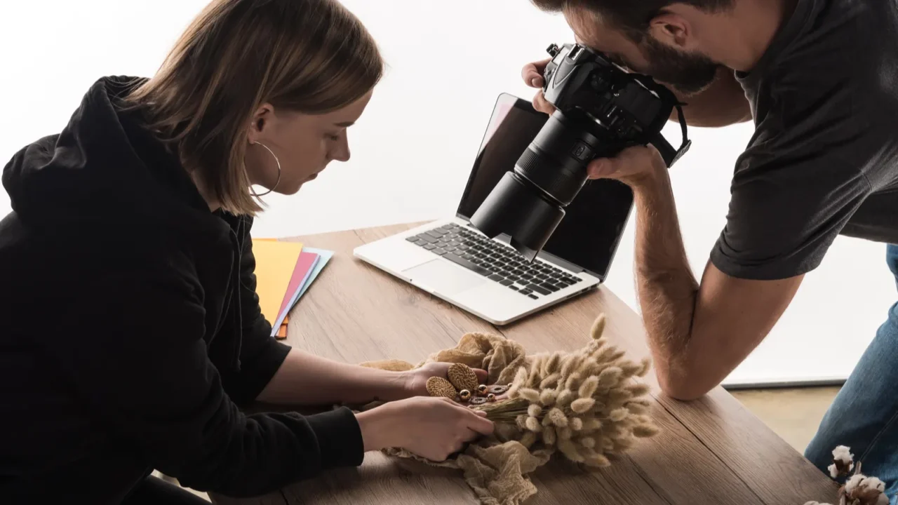 two commercial photographers take picture of composition with flora and jewelry on digital camera