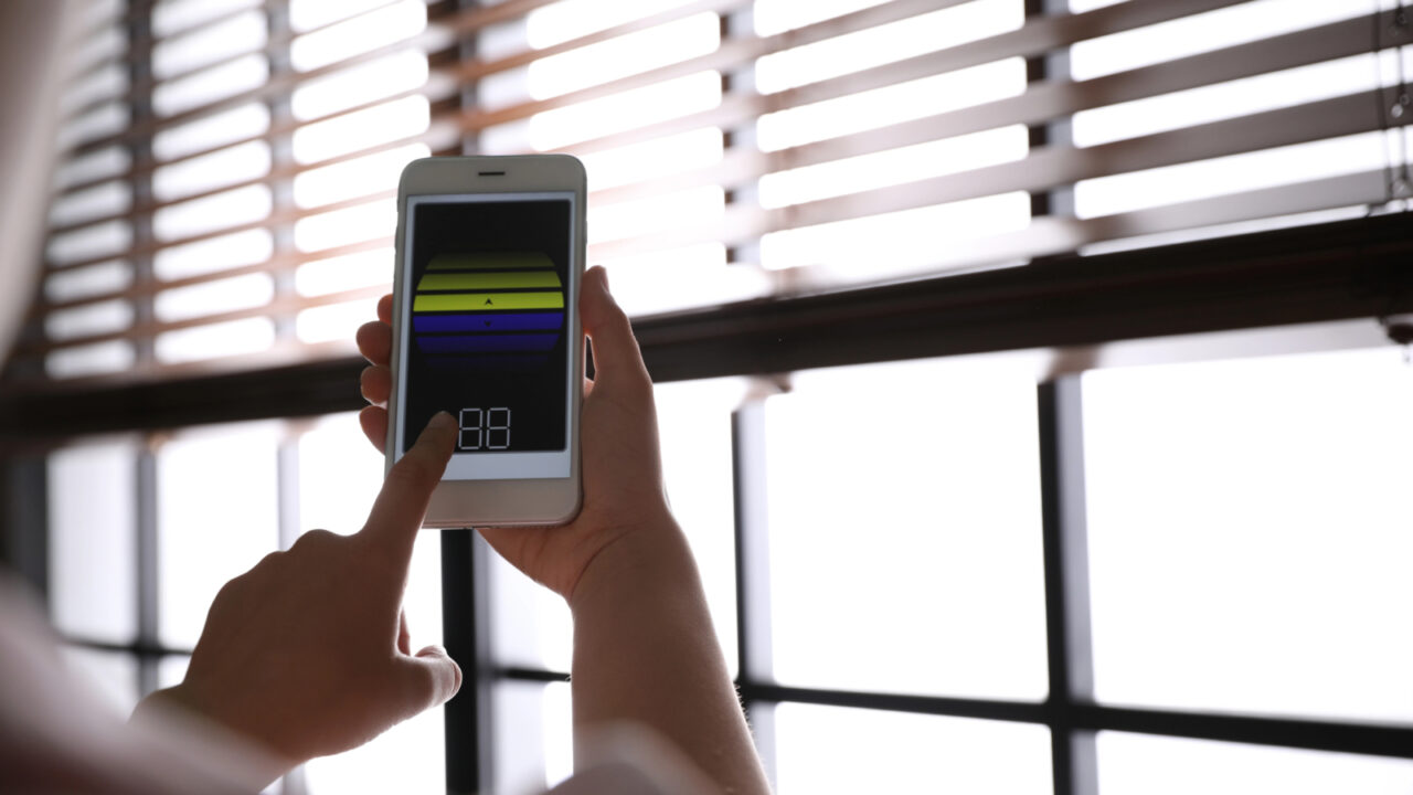 Woman using smart home application on phone to control window blinds indoors, closeup. Space for text