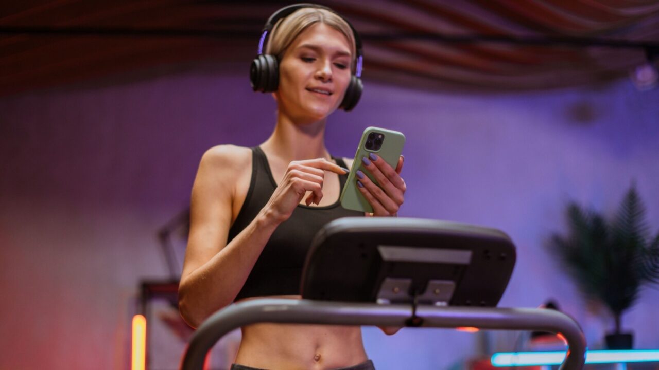 Woman working out o n treadmill while using her smart phone