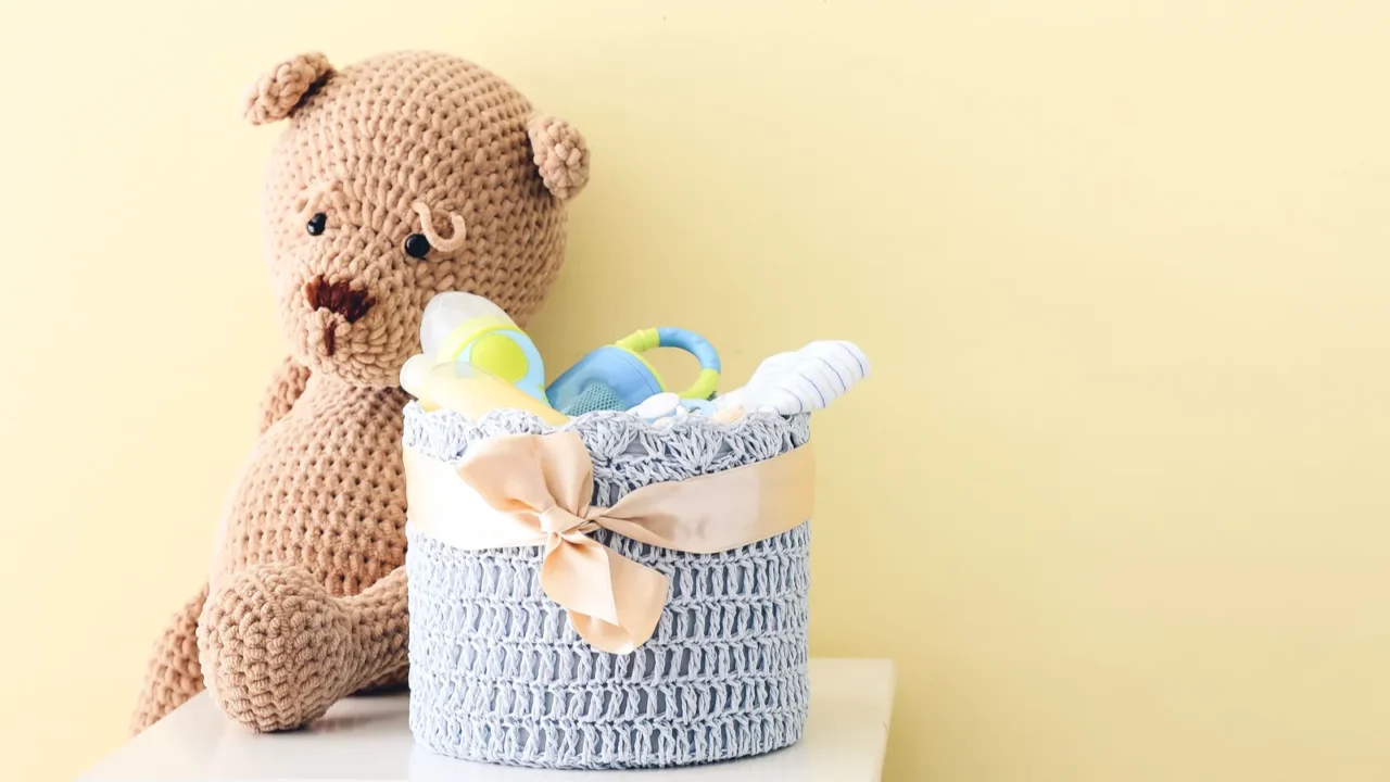 Basket with gifts for baby and teddy bear on table near color wall