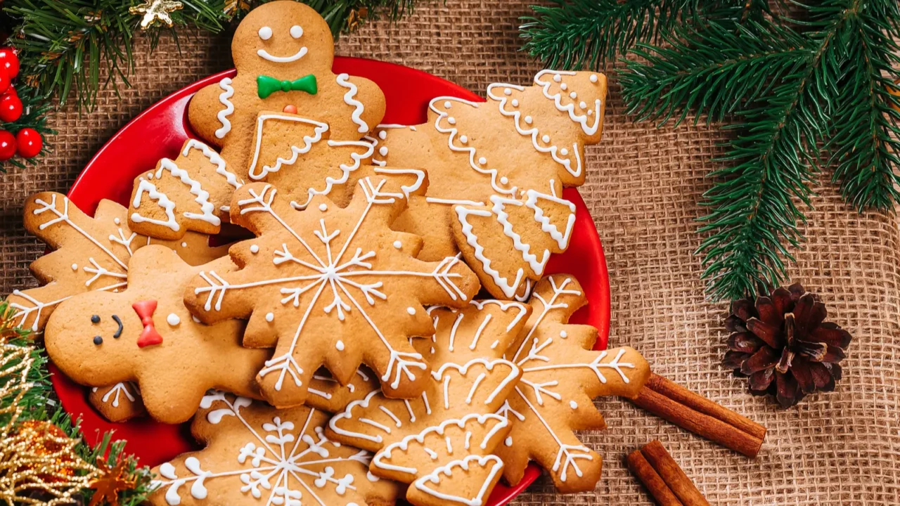 Christmas gingerbread cookies homemade in red plate with branches of Christmas tree and New Year decor on table with burlap tablecloth. Merry Christmas postcard.