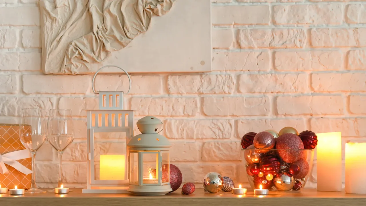 Christmas lanterns with glasses, gift and balls on shelf near white brick wall