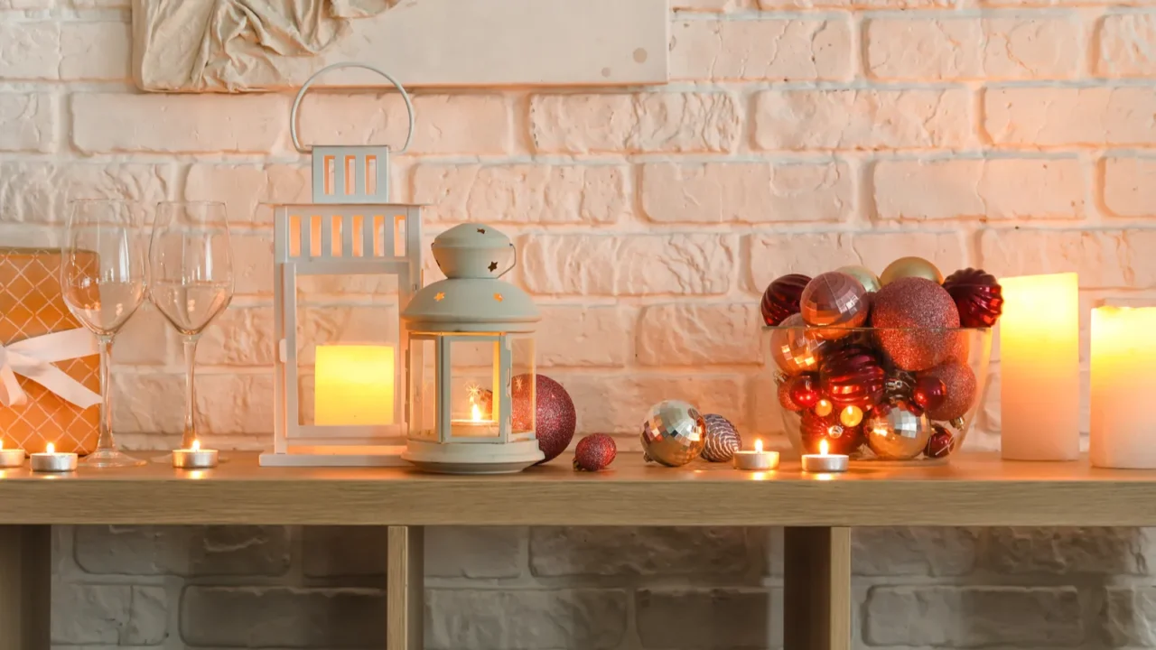 Christmas lanterns with glasses, gift and balls on shelf near white brick wall