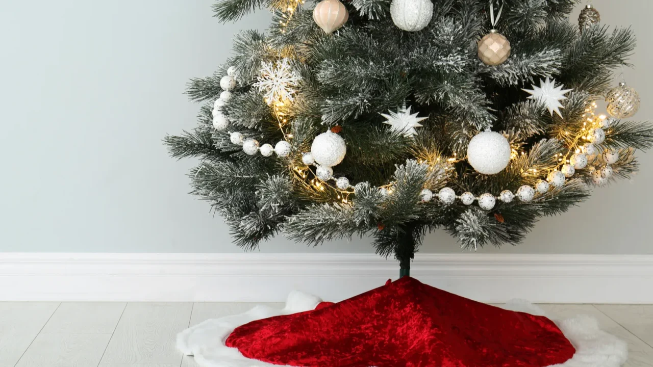 Decorated Christmas tree with red skirt indoors, space for text