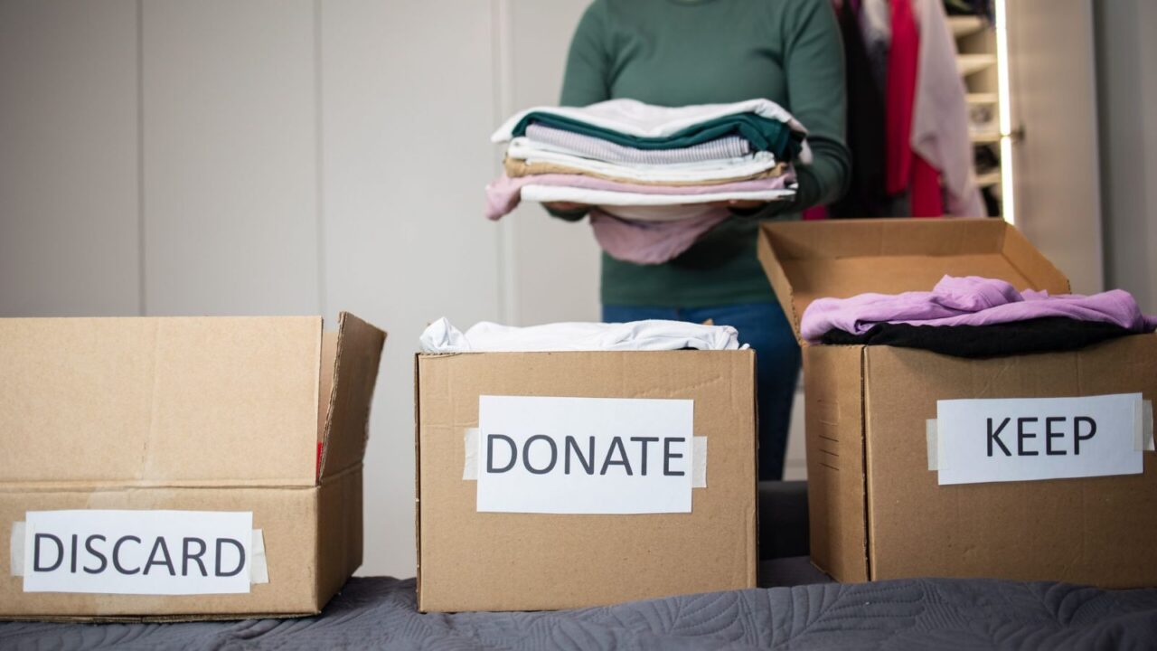 A woman sorting clothes in 3 boxes labelled "Discard" "Keep" and "Donate"