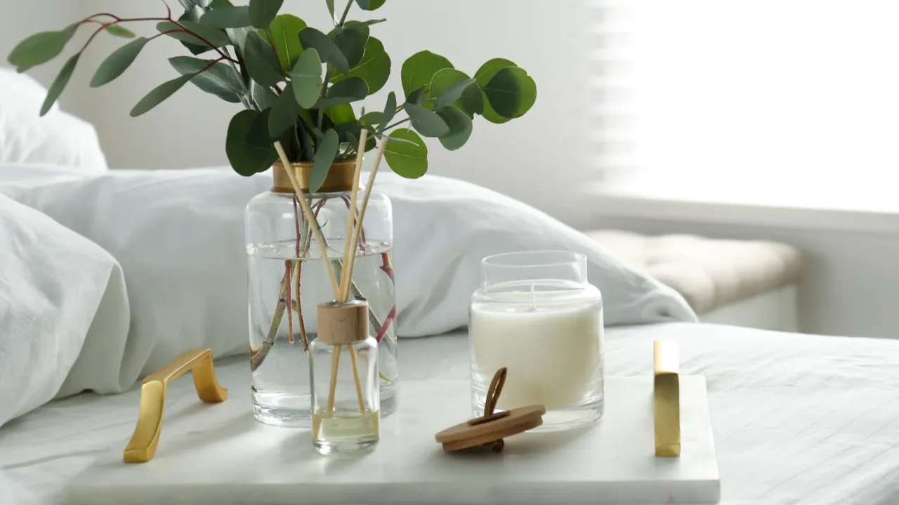 Eucalyptus branches, candle and aromatic reed air freshener on bed indoors, space for text. Interior elements