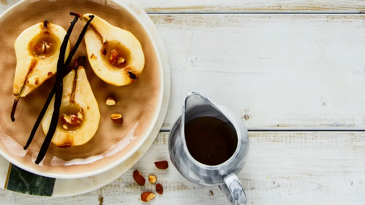 Flat-lay of delicious sweet pears baked with vanilla, maple syrup and almond on white wooden background. Top view.