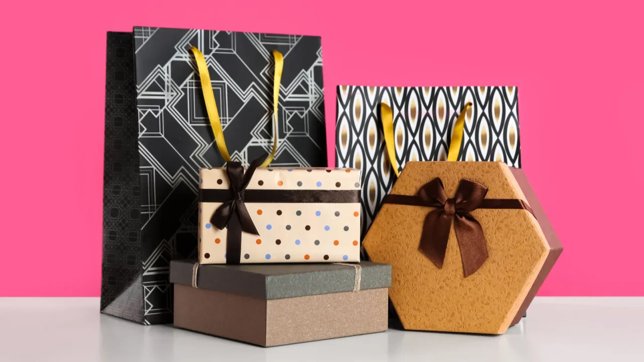 Gift bags and boxes on white table against pink background