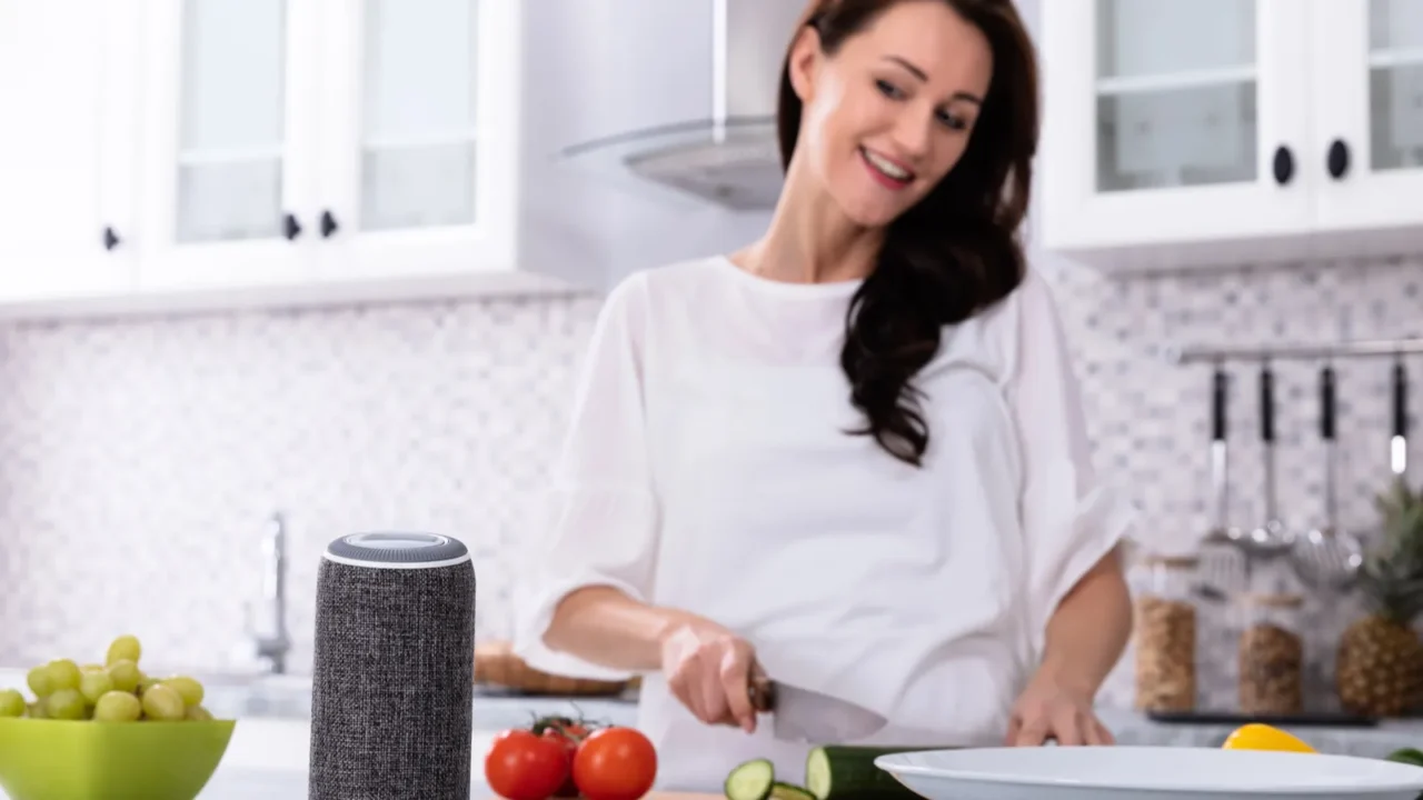 Happy Woman Talking To Voice Assistant While Slicing Cucumber With Kitchen Knife