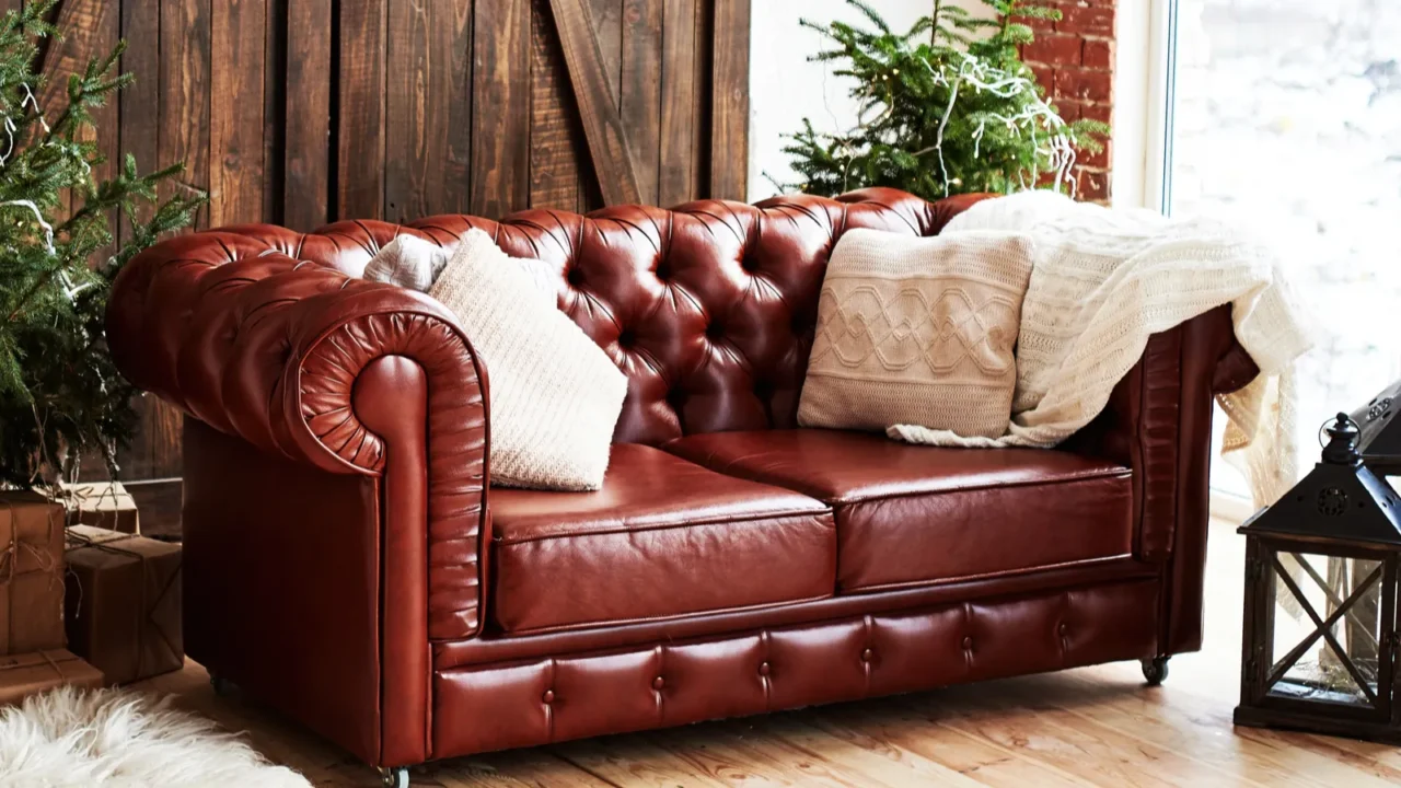 Leather vintage brown chesterfield sofa in Christmas interior with fir tree and gift boxes in loft room with wooden door and panoramic window, copy space