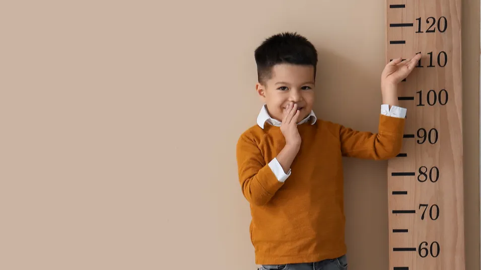 Little Asian boy measuring height near beige wall