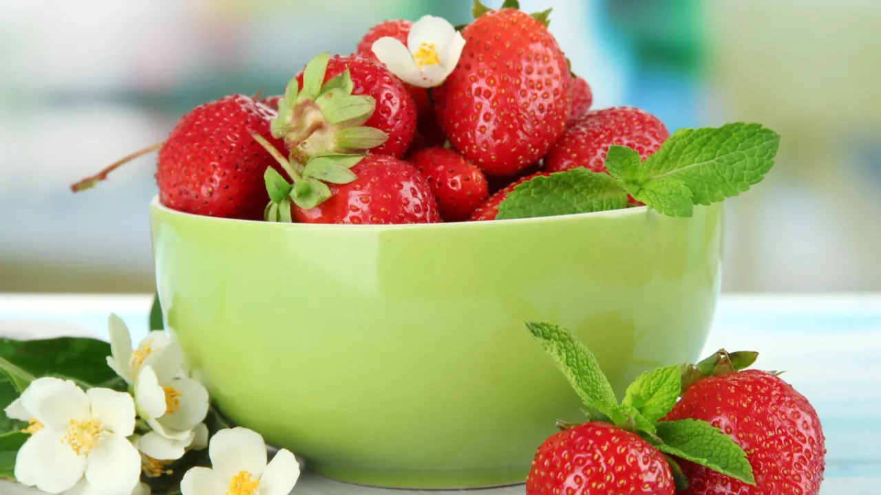 Ripe sweet strawberries in green bowl on blue wooden table