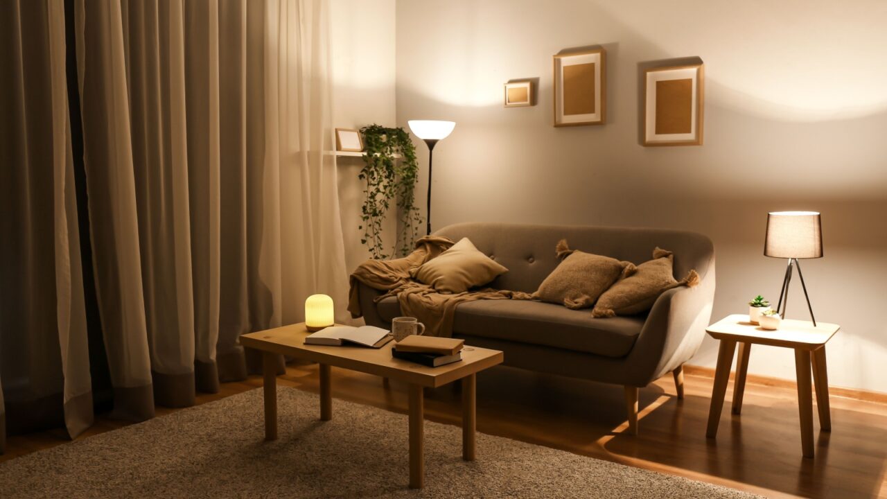 Night view of stylish interior of living room with sofa, coffee table, side table with lamp, floor lamp and curtains on window.